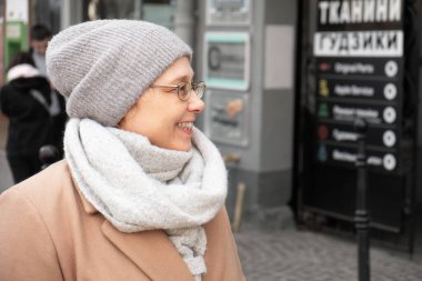 Şapkalı ve eşarplı kadın dışarıda gülümsüyor.