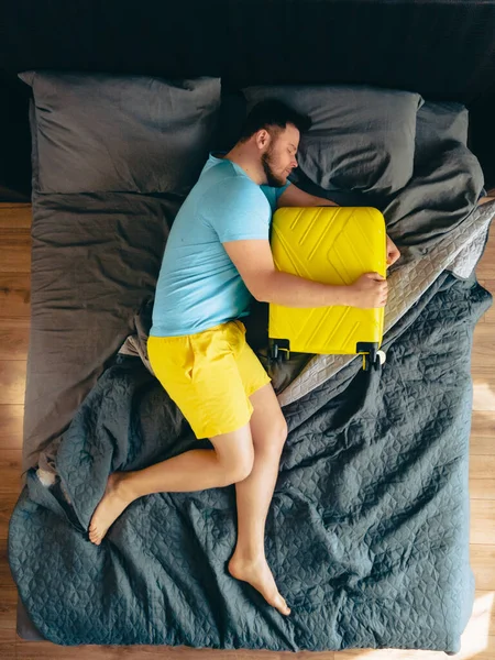Чоловік Мріє Про Відпустку Ліжку Обіймаючи Жовту Валізу Над Видом — стокове фото