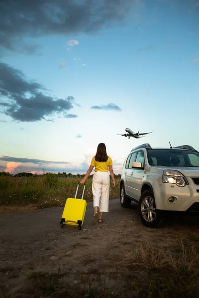 woman with luggage near white suv car plane in the air. copy space