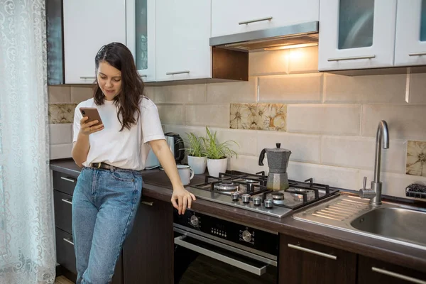 Frau trinkt Morgenkaffee in der Küche beim Internetsurfen am Telefon — Stockfoto