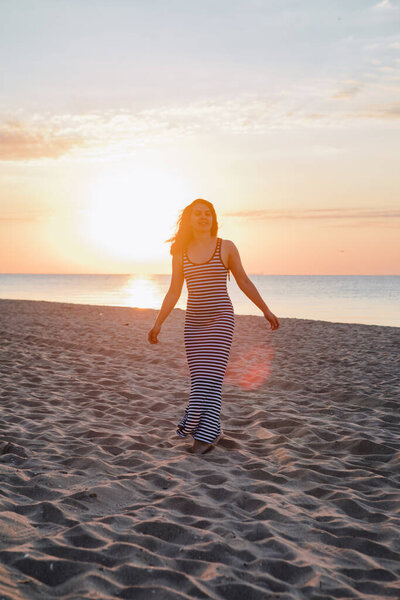 young beautiful sexy woman in dress walking bay sandy beach at sunset. summer vacation