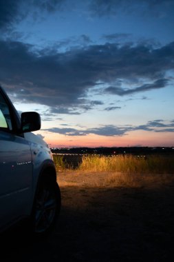 Gece sahasında arabanın farının manzarası. Arka planda akşam şehri. gün batımı