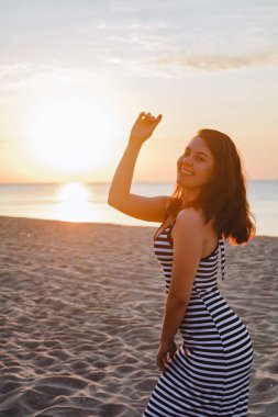 Gün batımında kumlu sahilde yürüyen güzel, seksi bir kadın.