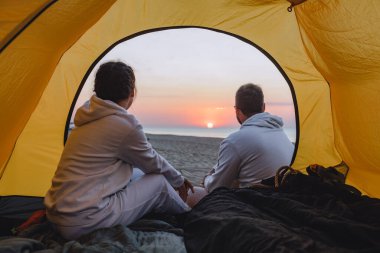 Kamp çadırında oturan çift gün batımını seyrediyor.