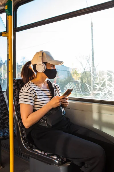 woman in medical mask at city tram public transport copy space evening soft light listening music with headset