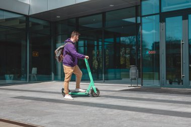 Genç adam ofis binasına elektrikli scooterla gidiyor. Kilometrelerce şehir yaşam tarzı.
