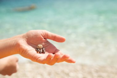 Kadın eli taş tutarken yakınlaşıyor. Arka planda deniz plajı. Boşluğu kopyala