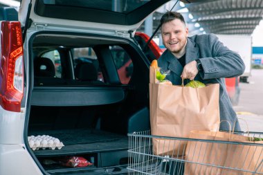 Adam arabanın bagajına mal dolu çantalar koyuyor.