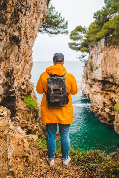 man in yellow raincoat standing on the cliff of canyon looking at stormy sea