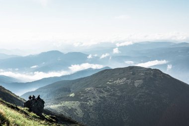 Pip Ivan, Ukrayna - 2 Ağustos 2020: Dağın tepesindeki kayanın tepesinde oturan üç kişinin arkadaşları panoramik manzaranın tadını çıkarıyorlar
