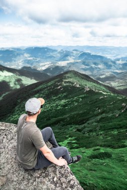 Genç ve güçlü bir adam dağın tepesindeki kayanın tepesinde oturmuş manzaranın tadını çıkarıyordu. yürüyüş kavramı