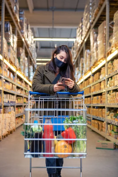 Frau Checkt Handy Beim Einkaufen Medizinischer Maske — Stockfoto