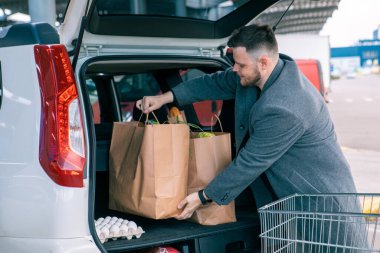 Adam arabanın bagajına mal dolu çantalar koyuyor.