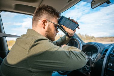 Telefonu olan üzgün adam arabada oturup fotokopi çekiyor.