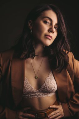 Kahverengi ceketli, stüdyo ışığı olan çekici genç bir kadının şehvetli portresi.