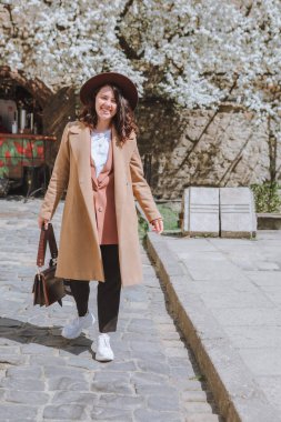 Gülümseyen, ceketli ve şapkalı güzel bir kadın. Arka planda, Spring City Caddesi 'nde yürüyen beyaz çiçek açan bir ağaç.