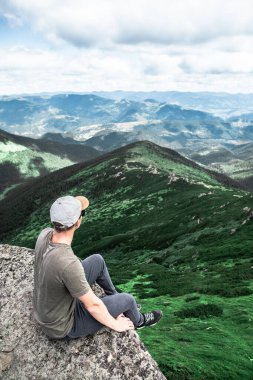 Genç ve güçlü bir adam dağın tepesindeki kayanın tepesinde oturmuş manzaranın tadını çıkarıyordu. yürüyüş kavramı