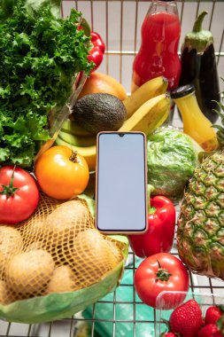 Market arabasında meyve ve sebzeli beyaz ekran fotokopi alanı olan bir telefon.
