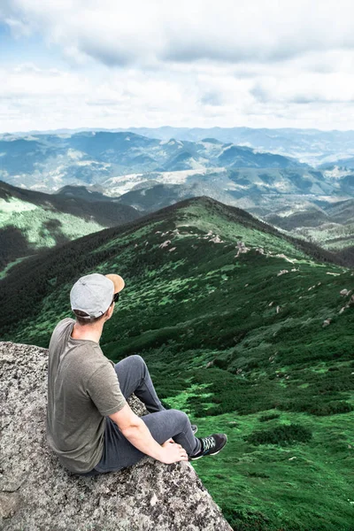 山の頂上の岩の上に座って景色を楽しんでいる若い男 ハイキングのコンセプト — ストック写真