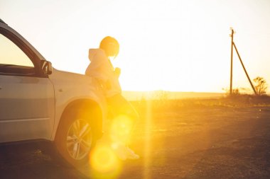 Kırsalda günbatımının tadını çıkaran bir kadın. Beyaz bir cipin yanında duruyordu. Yol gezisi