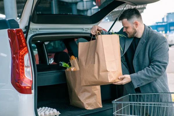 man putting bags with product in car trunk copy space
