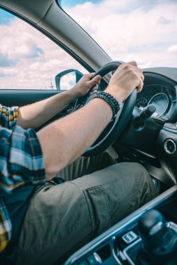 Adam ellerini direksiyona koyuyor. İçeriye bakıyor. Araba yolculuğu güneşli gün.