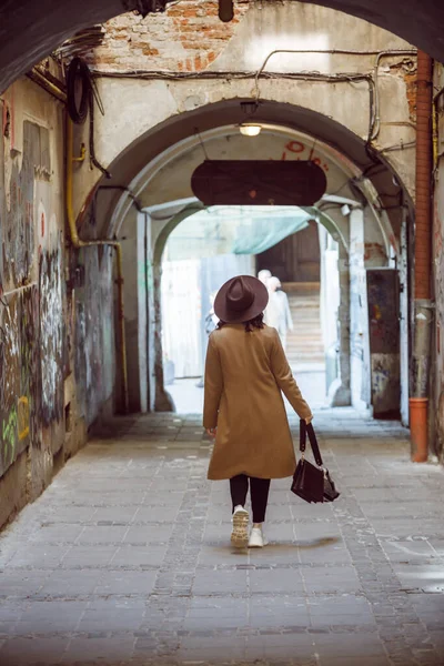 スタイリッシュなコートを着た女性と小さなヨーロッパの通りのコピースペースで歩く帽子 — ストック写真