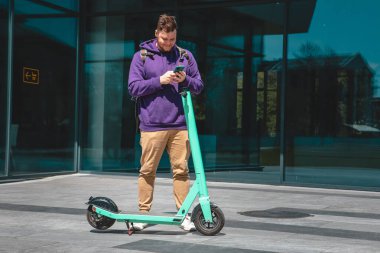 Genç adam ofis binasına elektrikli scooterla gidiyor. Kilometrelerce şehir yaşam tarzı.