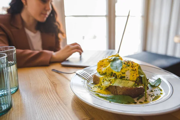 Mujer Trabajando Portátil Cafetería Comiendo Tostadas Vegetarianas Frescas Con Aguacate — Foto de Stock