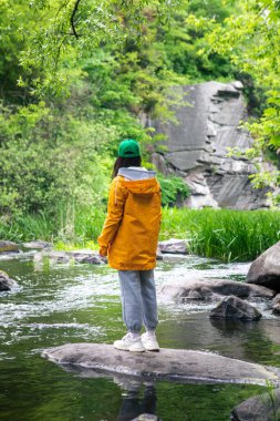 Sarı yağmurluklu yürüyüşçü kadın doğadaki kanyon güzelliğinin tadını çıkarıyor.