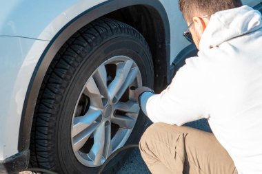 Adam araba lastiklerini kontrol ediyor.