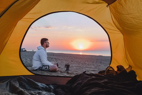 男が海の砂浜でコーヒーを作ってる 夏休みキャンプ テントを通して見る — ストック写真