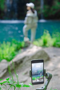 Kadın kendini telefonda vuruyor ve şelalenin fotokopi alanına bakıyor.