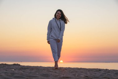 Gün doğumunda deniz kıyısında yürüyen gülümseyen genç bir kadın. Yaz seyahati