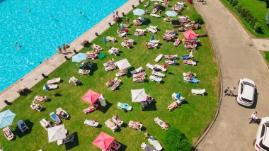 Güneşli yaz gününde şehir havuzunun yanında güneşlenen insanların hava görüntüsü.