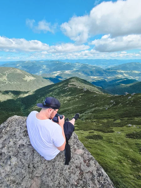 山の頂上の岩の上に座って景色を楽しんでいる若い男 ハイキングのコンセプト — ストック写真