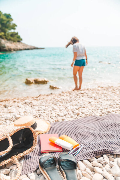 young pretty woman in summer outfit walking by sea shore blanket with beach stuff on blanket summer vacation