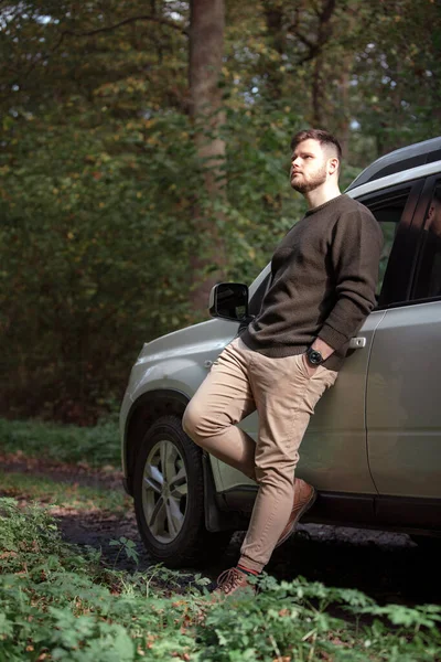 man standing near car in forest at trail road copy space. autumn season