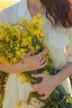 Bir demet kolza çiçeği kadının ellerinde. Yüzü görünmüyor.