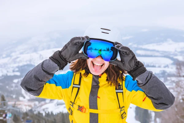 身穿滑雪服 头戴护目镜 头戴安全帽 面带微笑的年轻女子伸出舌头 — 图库照片