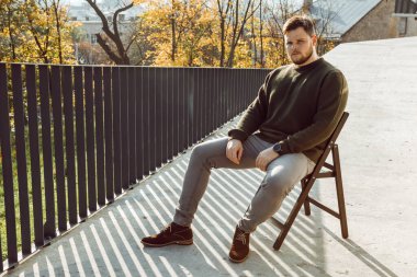 Acımasız yüzlü bir adam açık havada sandalyede oturuyor. Güneşli bir sonbahar günü fotokopi alanı.