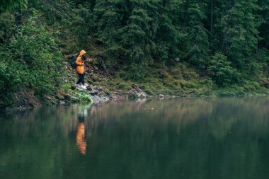 Göl kıyısında sarı yağmurluklu bir kadın yürüyüşçü.