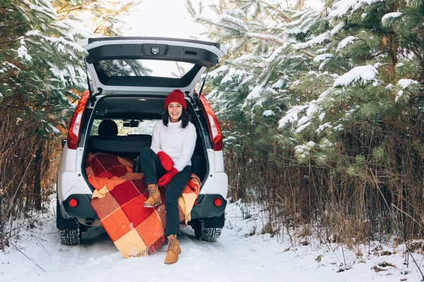 Χαμογελαστή όμορφη γυναίκα στο πορτ-μπαγκάζ του αυτοκινήτου στο χιονισμένο δάσος του χειμώνα — Φωτογραφία Αρχείου
