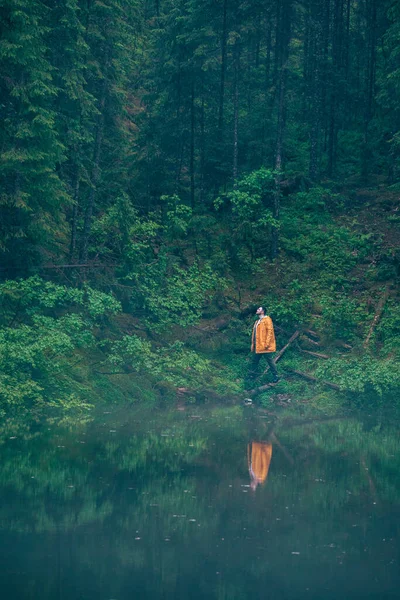 Uomo escursionista in impermeabile giallo guardando lago di montagna — Foto Stock