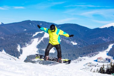 Yeşil ceketli bir adam snowboard 'la zıplıyor. Kış dağları seyahat