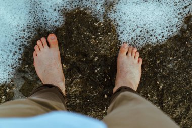 Tepeden çıplak ayaklı adam deniz taşlı sahilde yürüyor. Boşluğu kopyala