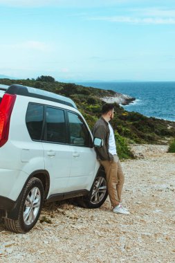 Adam arazi aracına yaslanıp deniz manzarasının keyfini çıkarıyor. Yaz tatili. yaşam tarzı konsepti
