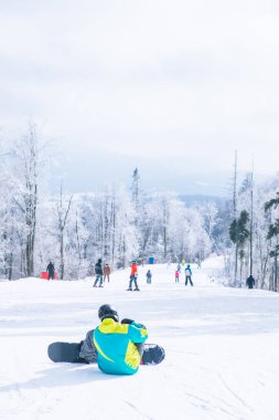 Tepede oturan adam manzaranın tadını çıkarıyor. Snowboard. Kış sporları. Boşluğu kopyala