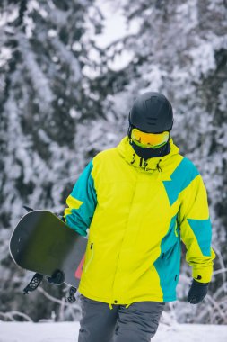 Snowboard 'lu bir adam karlı tepenin yanından geçiyor.