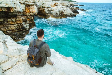 sırt çantası ile adam şehir manzarası zevk uçurumun üzerinde oturan. yaz tatili